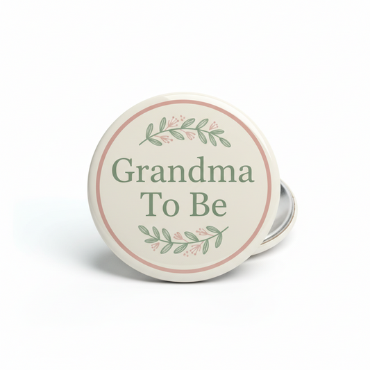 Round pinback button, beige face with pink rim, green “Grandma To Be” and leaf accents