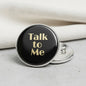Black round pinback button with 'Talk to Me' gold lettering