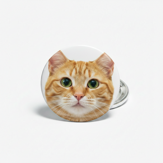 A round pinback button badge featuring a cute cartoon yellow kitten face with green eyes, pink ears, and black outlines, shown on a light gray background.